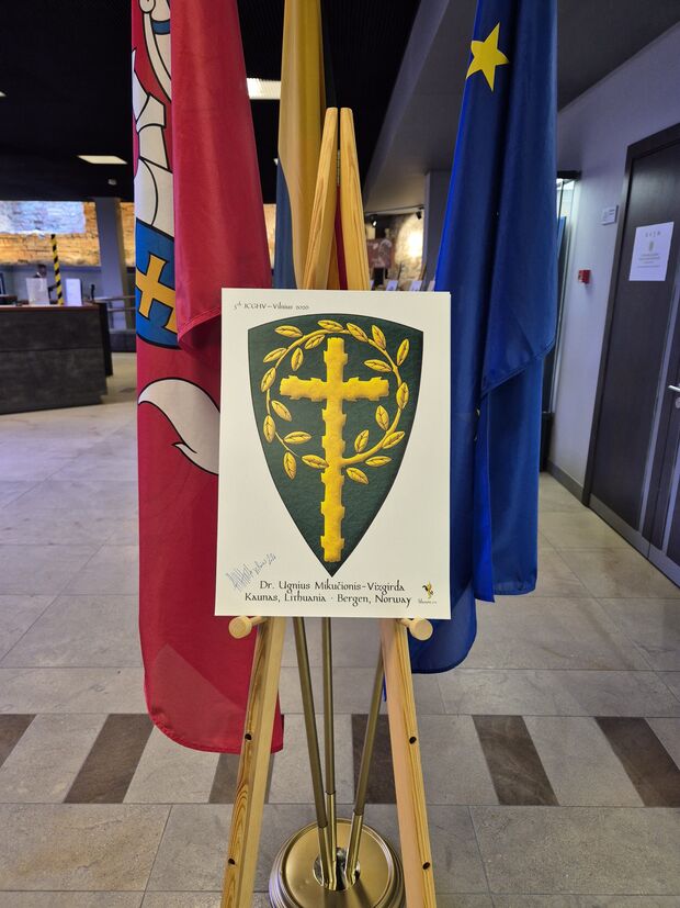 Vert, a Latin cross, raguly, issuant from its sinister a leaved offshoot encircling the cross, its end terminating and debruising the lower limb Or.
